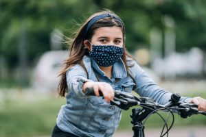 Young girl riding a bicycle with a mask